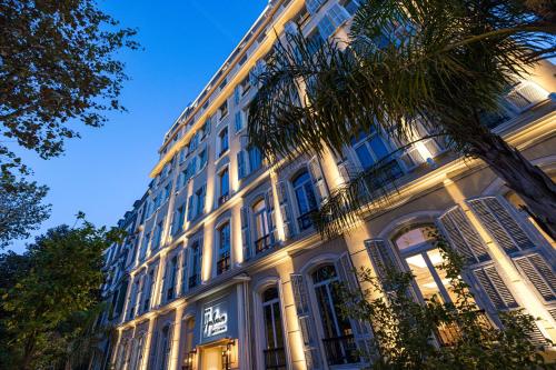 a large white building with a palm tree in front of it at Hôtel Apollinaire Nice in Nice