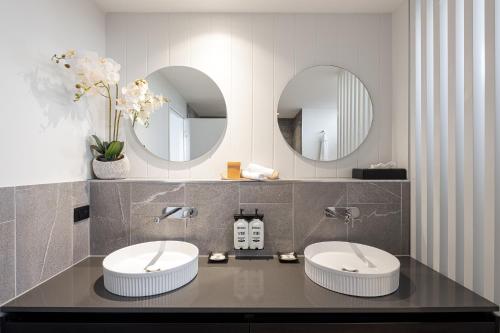 a bathroom with two sinks and two mirrors at The Sebel Brisbane Margate Beach in Redcliffe