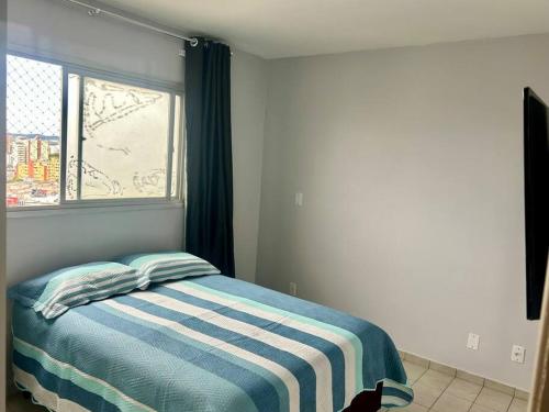 a bedroom with a bed with a striped blanket and a window at Ap de 2 q, 70 metros, em bairro nobre e central in Goiânia