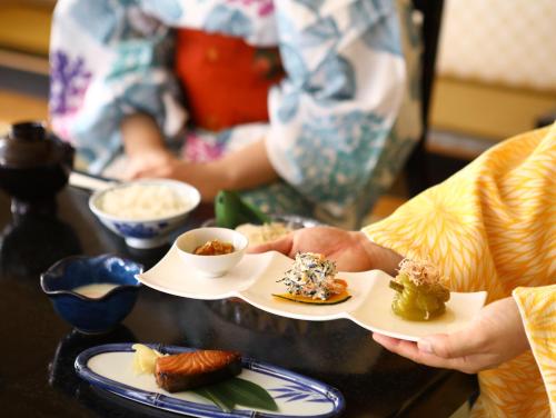 eine Person, die zwei Teller mit Lebensmitteln auf einem Tisch hält in der Unterkunft Ogiwarakan in Chikuma
