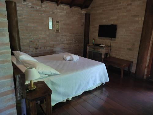 1 dormitorio con 1 cama blanca y TV en Pássaro de Fogo, en Santo Antônio do Pinhal