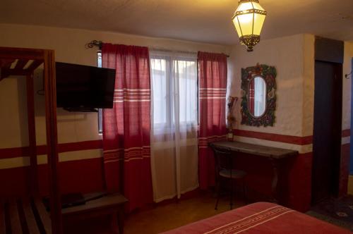 een slaapkamer met rode gordijnen, een bureau en een televisie bij Posada del Fraile in Tepotzotlán