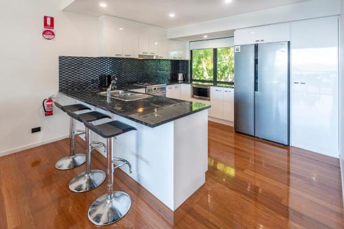 a kitchen with white cabinets and a counter with stools at Pinnacle Apartments on Hamilton Island by HIHA in Hamilton Island