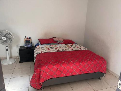 Descansa con tranquilidad في فيلافيسينسيو: غرفة نوم بسرير لحاف احمر ومروحة