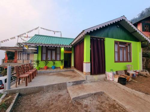 a green house with chairs in front of it at Neoravalley Homestay, Icche Gaon in Pedong