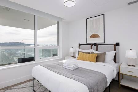 a white bedroom with a large bed and a window at Luxury Oceanfront 1BR condo at Lions Gate in North Vancouver