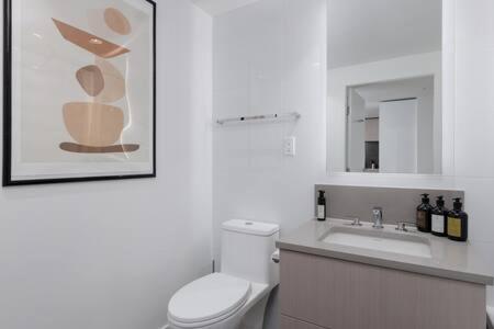 a white bathroom with a toilet and a sink at Luxury Oceanfront 1BR condo at Lions Gate in North Vancouver