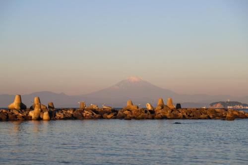 a mountain in the background with rocks in the water at StellaStoria HAYAMA Seaside house with open-air bath in Hayama