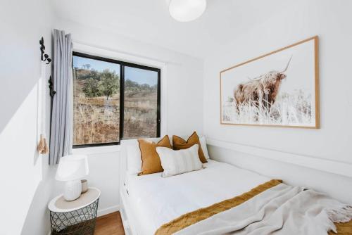a white bedroom with a bed and a window at Canguri Boutique - A Memorable Farmstay near Mudgee in Mudgee