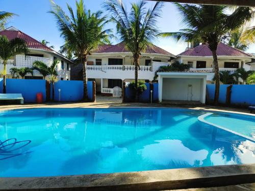 a swimming pool in front of a house with palm trees at Kimbi's Villa in Ukunda