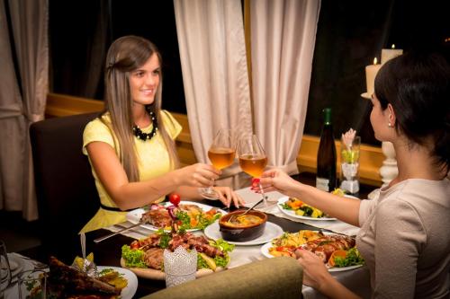 two women sitting at a table with food and wine at Hotel Danica in Vrnjačka Banja