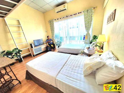 a bedroom with a large bed and a man sitting in a room at EZ Sleep @ Ratchada 19 in Bangkok
