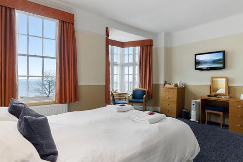 a hotel room with a bed and a desk and window at Babbacombe Royal Hotel and Carvery in Torquay