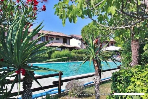 una piscina con due palme di fronte a una casa di Marina Punta Verde a Lignano Sabbiadoro
