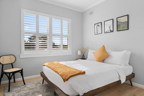 een witte slaapkamer met een bed en een stoel bij Ocean's Embrace - A Local's Haven at Bondi Beach in Sydney