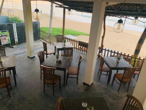 ein Restaurant mit Tischen und Stühlen und einem Strand in der Unterkunft Tamaro Beach Resort in Hikkaduwa