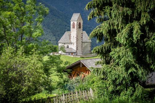 a church on a hill with a fence and trees at Oberpiskoihof in Funes