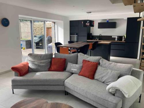 uma sala de estar com um sofá cinzento com almofadas vermelhas em Jolie maison binicaise em Gicquel