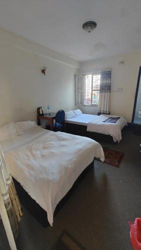 a bedroom with two beds and a desk and a window at Hotel Mansarovar in Dailekh