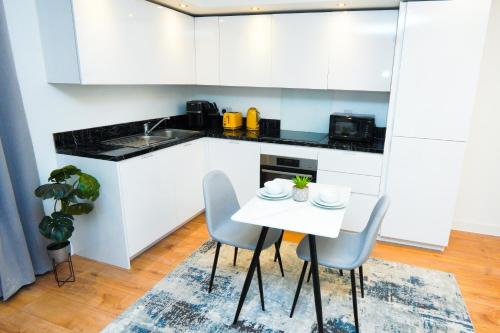 a kitchen with white cabinets and a white table and chairs at Stylish Airport Apartment in Luton