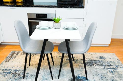 a white dining room table with two chairs at Stylish Airport Apartment in Luton