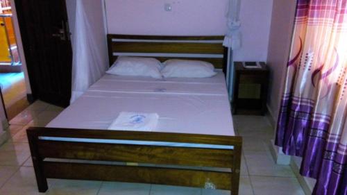 een klein bed met een houten frame en witte lakens bij Checkpoint Inn Hotel, Mombasa in Mombasa