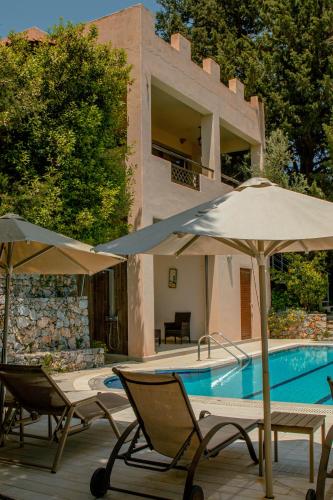 a pool with chairs and umbrellas next to a house at Villa Kalamitsi Luxury Villa in Apokorona Chania in Kariá