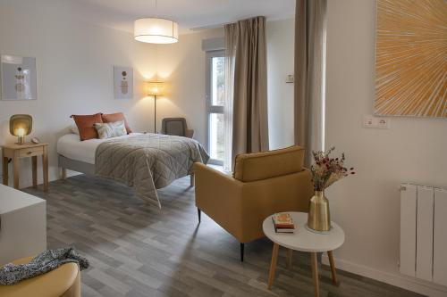 a bedroom with a bed and a chair and a table at DOMITYS LES SEQUANES in Chalon-sur-Saône