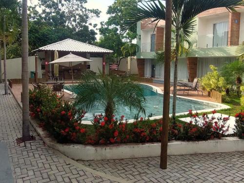 a swimming pool with flowers in front of a house at Vilage Aconchegante - Imbassaí in Imbassai