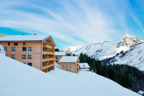 a building in the snow with mountains in the background at Alpenstolz Damüls Haus 2 - Stilvoll urlauben in den Bergen in Damuls