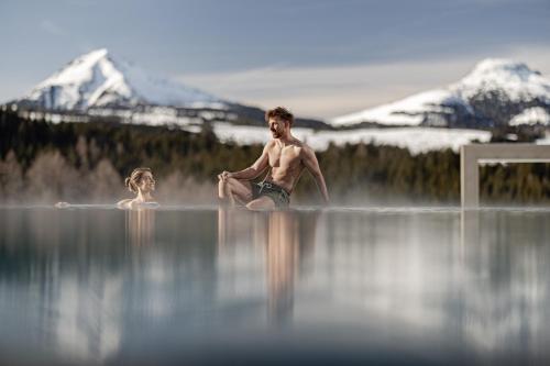 a man and a woman swimming in a body of water at Sporthotel Obereggen in Obereggen