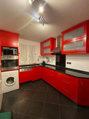 - une cuisine avec des placards rouges et un lave-linge dans l'établissement Rez de jardin - JO 2024, à Plaisir