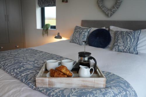 a tray with cups and croissants on a bed at The Angel - Luxury Lakeside Lodge in Cotham