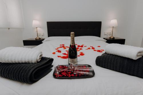 Una botella de champán en una cama con flores rojas en Excapada suite de Murcia, en Murcia