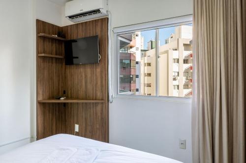 een slaapkamer met een bed en een raam met een tv bij Apto confortável a 4min do mar RTA042 in Balneário Camboriú