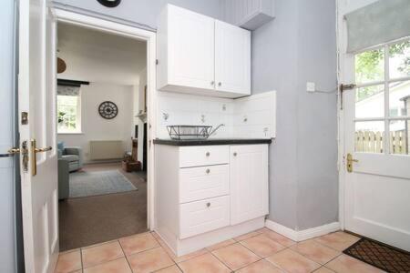 a kitchen with white cabinets and a door to a room at The Cornish Nook by StayStaycations in Camelford