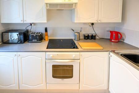 cocina con armarios blancos y fogones en Ellan Hay by StayStaycations en Bristol