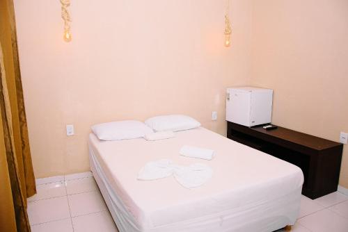 Schlafzimmer mit einem Bett mit weißer Bettwäsche und einem Kühlschrank in der Unterkunft Pousada do gaúcho in Barreirinhas