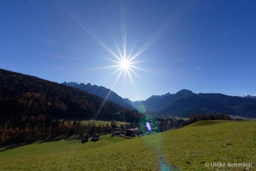 a sun shining on a green hill with mountains in the background at Appartment Lanz in Dobbiaco