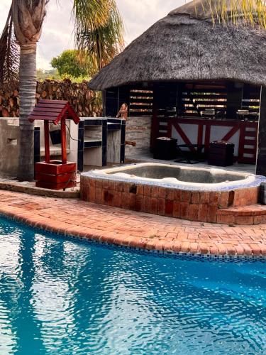 a swimming pool next to a hut with a thatch roof at immaculate 5 bedroomed house in Bulawayo