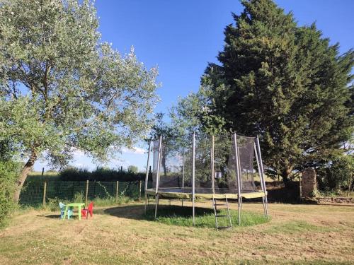 a metal swing set in a field with trees at Roulotte équipée - Gite La Pâquerie in Le Louroux-Béconnais