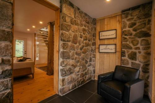 a room with a stone wall and a leather chair at Le Repere Etoile au coeur de la nature in Sainte-Lucie-de-Doncaster