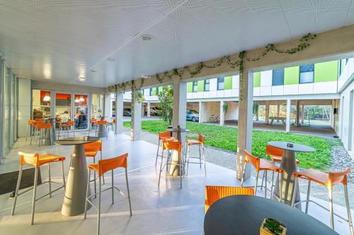 un restaurant avec des chaises orange, des tables et des fenêtres dans l'établissement Montempô Apparthôtel Toulouse Balma, à Toulouse