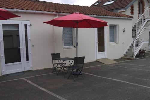 een patio met een tafel en stoelen en een rode parasol bij Appartement 27 Groix in La Bernerie-en-Retz