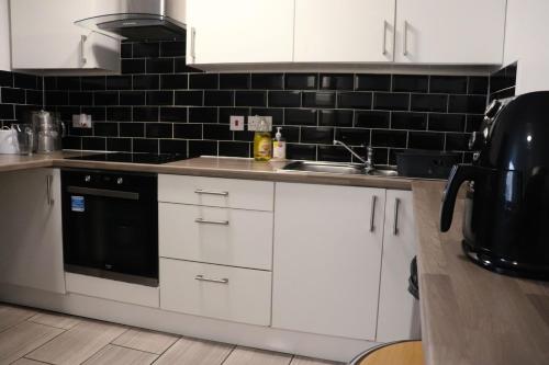 a kitchen with white cabinets and a black tile wall at Kop View in Liverpool