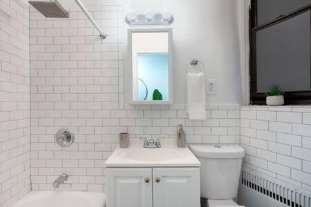 La salle de bains blanche est pourvue d'un lavabo, de toilettes et d'un miroir. dans l'établissement 91-2A Stylish 3BR 2Bth with W D, à New York