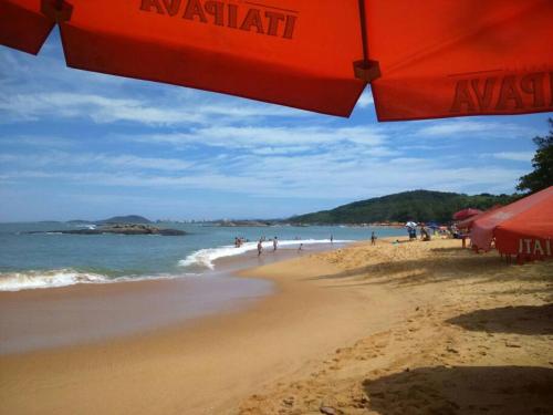 a beach with a red umbrella and people in the water at Temporada Praia de Setiba in Guarapari