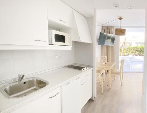 cocina blanca con fregadero y mesa en Apartamentos Morito Beach en Cala Millor