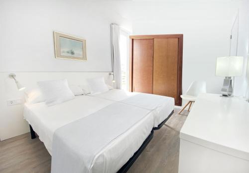 a white bedroom with a bed and a table at Apartamentos Morito Beach in Cala Millor