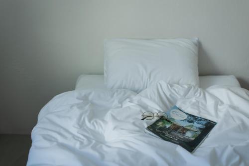 a white bed with a book and glasses on it at Square 8 HAKUBA RETREAT by UNPLAN in Hakuba